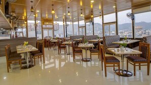 Un restaurant doté de plusieurs espaces de restauration, comprenant des tables et des banquettes, et offrant une vue sur la ville grâce à de grandes fenêtres.