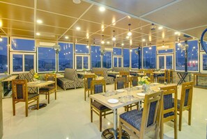 Ein Restaurant mit mehreren Tischen und Stühlen, großen Fenstern und Deckenventilatoren.