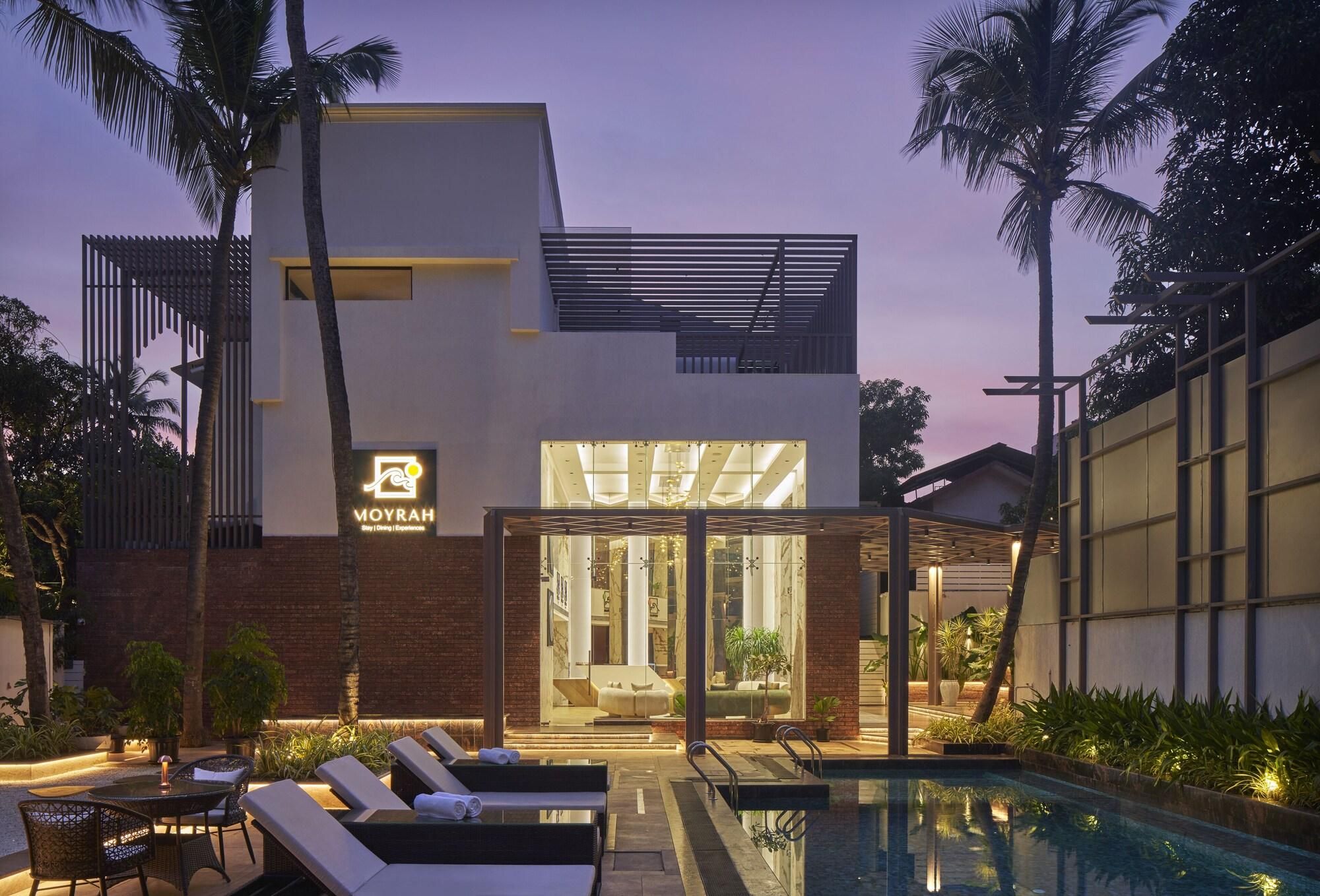 A modern building with a pool, lounge chairs, and palm trees.