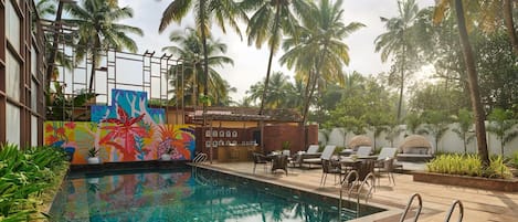 Uma piscina com água cristalina, rodeada por palmeiras e um mural colorido.