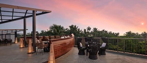 Um deck de madeira com móveis de vime e um espaço de bar com vista para palmeiras.