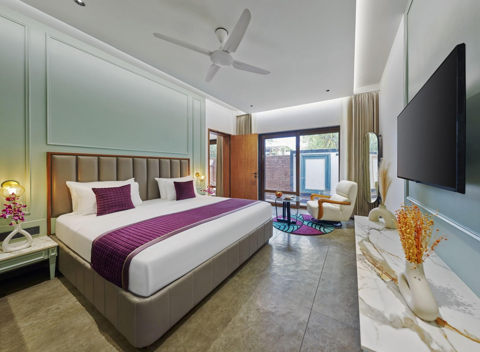 A modern hotel room with a large bed, a ceiling fan, a TV, a seating area with a table and chairs, and a large window.