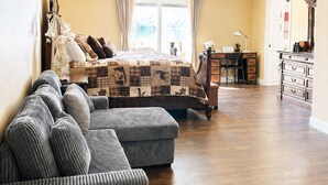 Um quarto espaçoso com uma cama grande, uma mesa de trabalho e uma cadeira, um ventilador de teto e vista para o exterior.