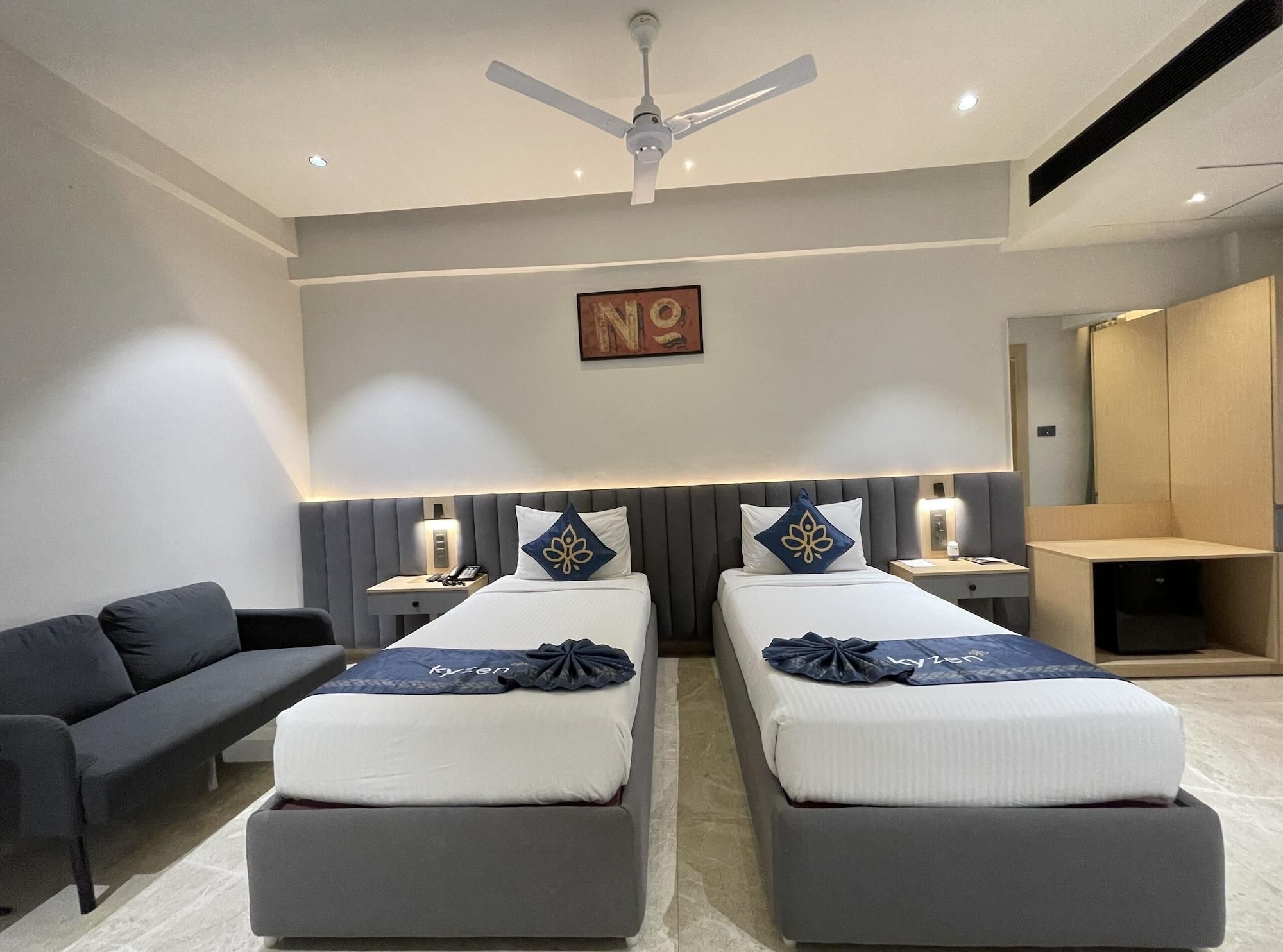 Ein modernes Hotelzimmer mit zwei Betten, einem Schlafsofa, einem Deckenventilator, einem Gemälde und einem Kleiderschrank.