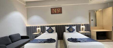 Ein modernes Hotelzimmer mit zwei Betten, einem Schlafsofa, einem Deckenventilator, einem Gemälde und einem Kleiderschrank.