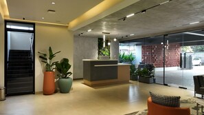 A reception area with a counter, potted plants, a staircase, and a glass door leading outside. - Hotel Kyzen (Hyderabad)