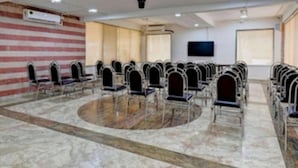 A conference room with rows of chairs, a marble floor, a mounted television, and an air conditioning unit on the wall. - Doves Kohinoor Exotica- Lonavala (Mawal)