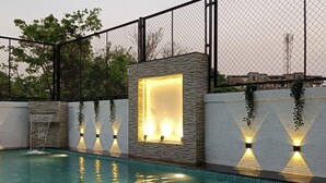 A swimming pool with a stone wall and a fence. - Doves Kohinoor Exotica- Lonavala (Mawal)