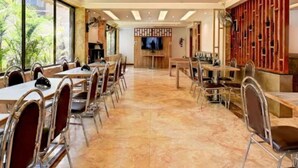 A spacious dining area with multiple tables and chairs, a television in the background, and a view of greenery outside. - Doves Kohinoor Exotica- Lonavala (Mawal)