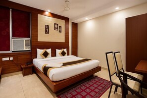 A hotel room with a wooden bed, a red patterned rug, a desk, and a chair. - Amaira Hotels And Banquets (Ghaziabad)