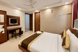 Habitación de hotel con cama, escritorio, silla, televisor y puerta de baño.