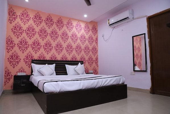 A bedroom with a bed, a nightstand, an air conditioning unit, and a mirror on the wall. - Hotel Axiom Prime (Lucknow)