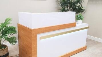 A reception desk with a wooden base and white top, flanked by potted plants.