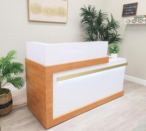 A reception desk with a wooden base and white top, flanked by potted plants.