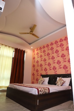 A bedroom with a bed, a ceiling fan, and a wall with a floral pattern. - Hotel Axiom Prime (Lucknow)