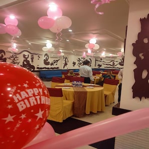 A restaurant with round tables, balloons, and a wall mural. - Hotel Comfort Inn Bl (Haldwani)