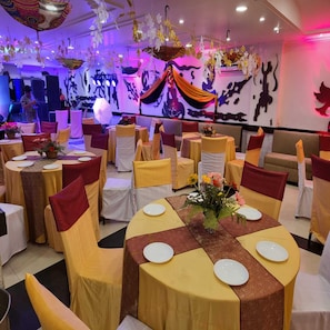 A banquet hall with round tables, chairs, and hanging decorations. - Hotel Comfort Inn Bl (Haldwani)