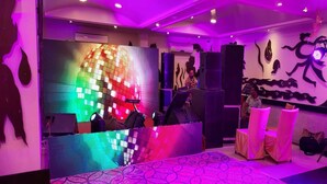 Um quarto com uma bola de discoteca colorida, um espaço para DJ e um tapete estampado.