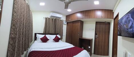 A hotel room with a bed, a TV, a wardrobe, and an air conditioning unit.