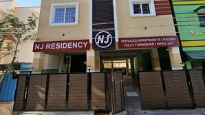 En byggnad med flera våningar, med en skylt som visar texten ”NJ RESIDENCY” och ”FULLT MÖBLERADE SERVICEBOSTÄDER | ÖPPET DYGNET RUNT”.