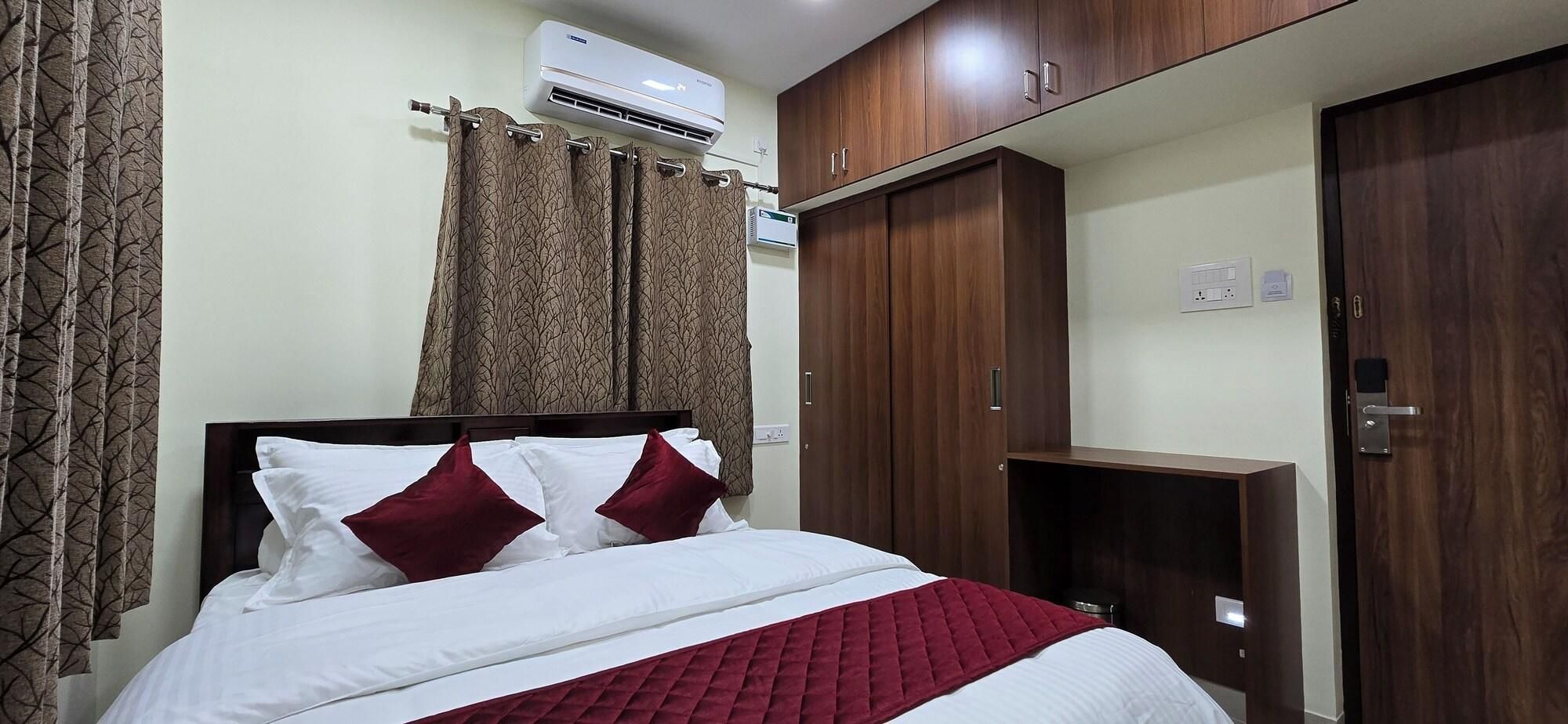 A hotel room with a bed, curtains, an air conditioning unit, wooden cabinets, and a wardrobe.