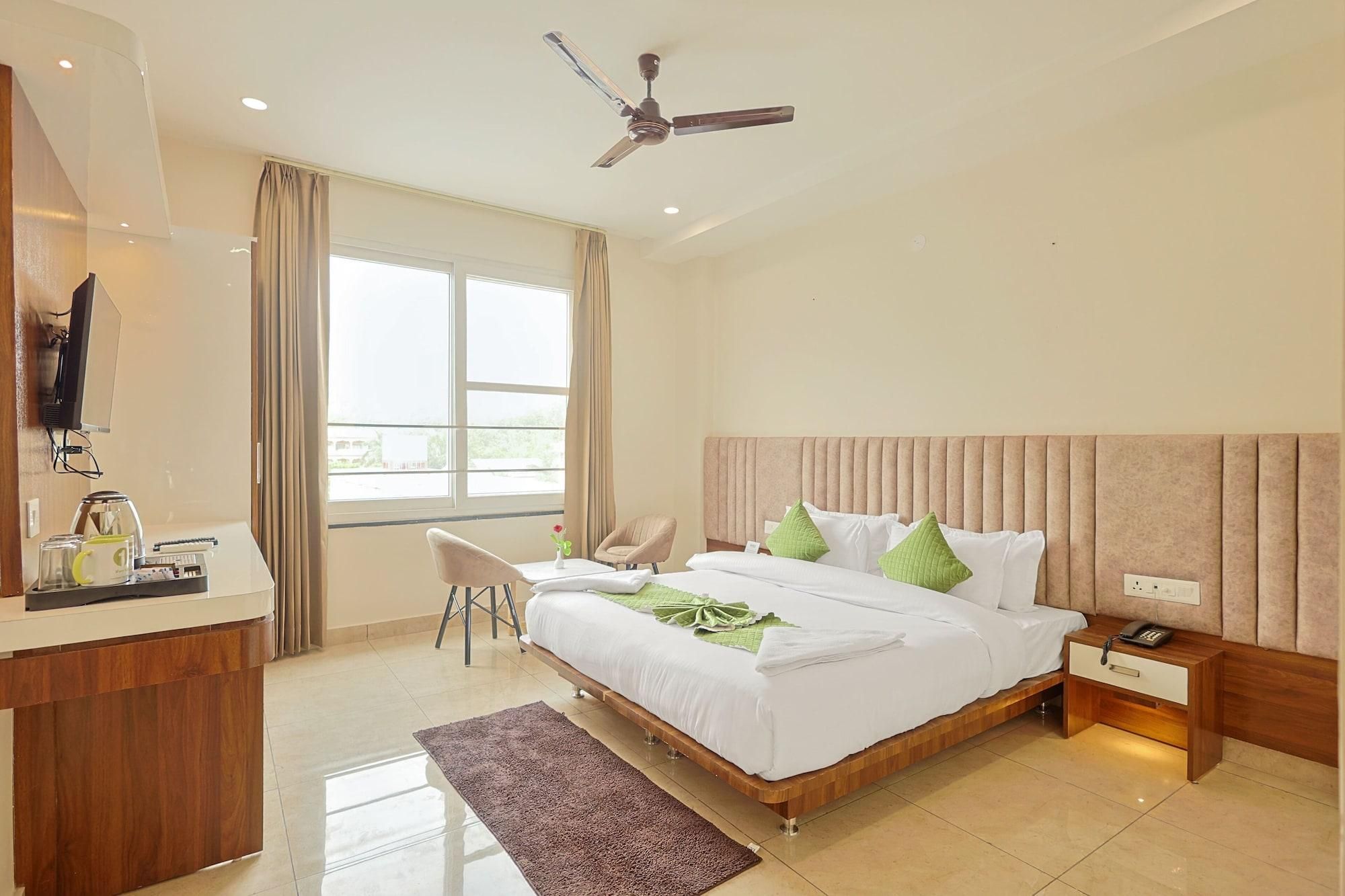 Habitación de hotel con cama, mesita de noche, silla, escritorio con teléfono y ventilador de techo.