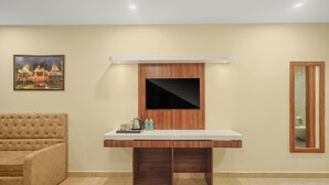 Ein modernes Zimmer mit Fernseher an der Wand, einer gepolsterten Couch und einem kleinen Tisch mit Wasserkocher und Wasserflaschen.