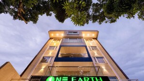Ein Hotel namens 'NE EARTH ELEGANT' mit modernem architektonischem Design, mehreren Stockwerken und einer gut sichtbaren, beleuchteten Werbetafel.