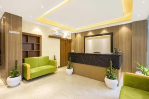 A reception area with a black marble counter, green sofas, wooden paneling, and potted plants. - One Earth Elegant (Yamkeshwar)