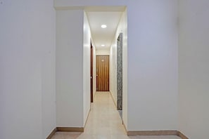 Ein schmaler Flur mit einer Holztür am Ende, weißen Wänden und einem gefliesten Boden.