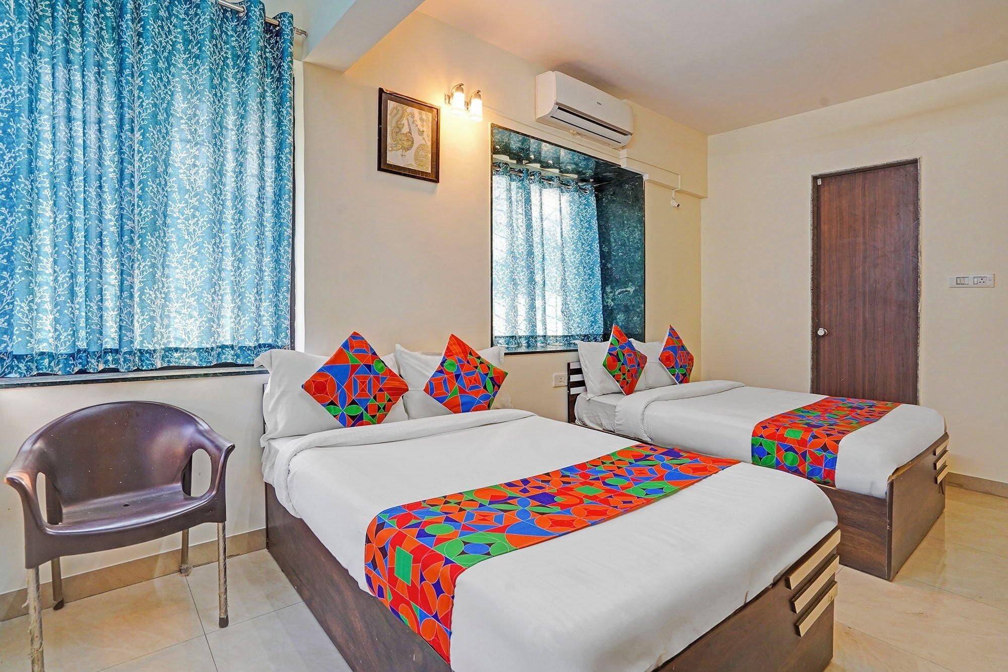 A hotel room with two beds, a chair, a window with curtains, an air conditioning unit, and a door.