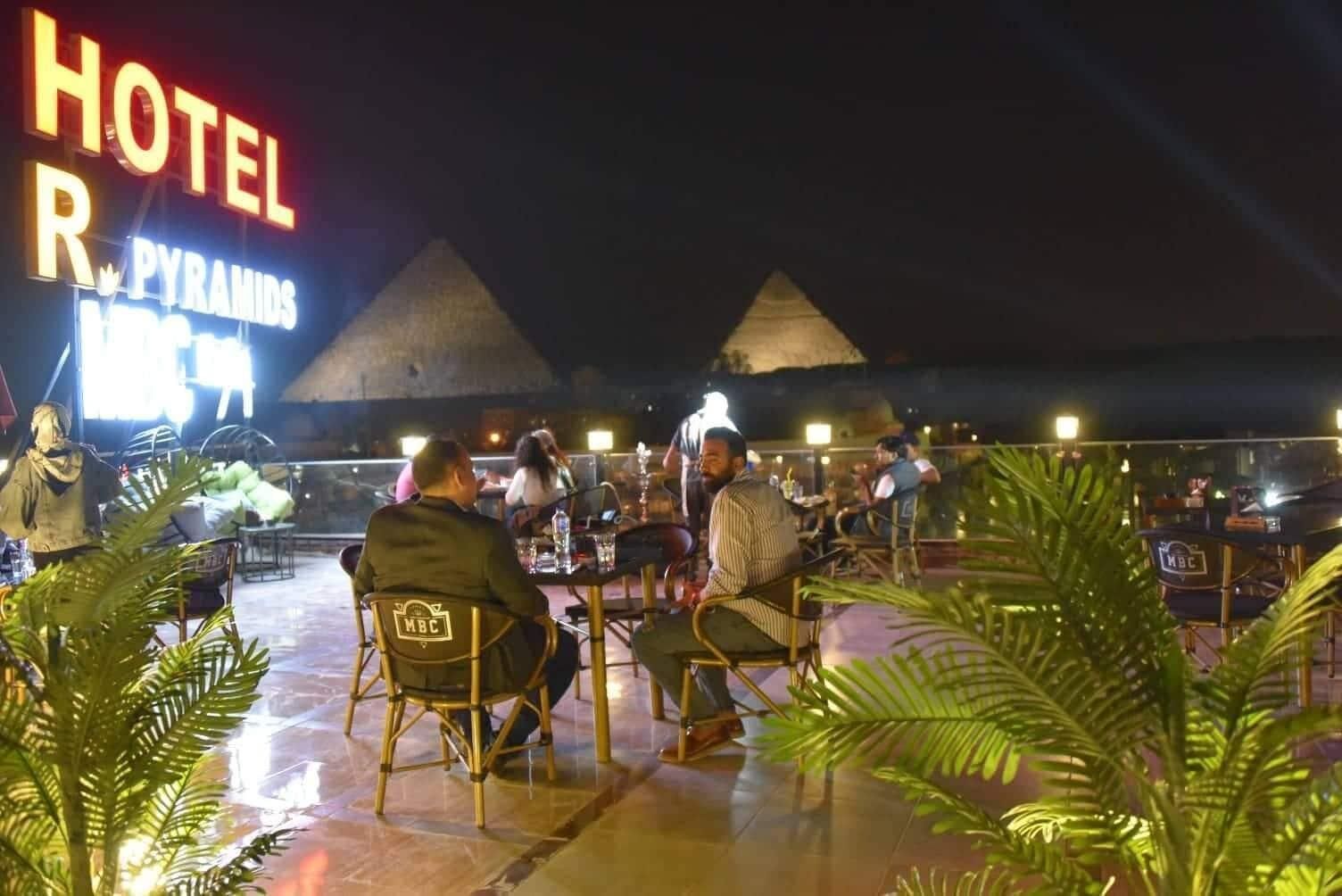 Un hotel llamado 'HOTEL R. PYRAMIDS' con terraza al aire libre y vistas a las pirámides al fondo.