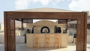 A wooden pergola structure with a bar area underneath, featuring a counter and three stools. - Guest House Pyramids View (Giza)