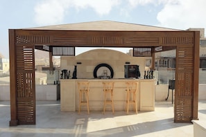 Une structure de pergola en bois abritant un espace bar, avec un comptoir et trois tabourets.