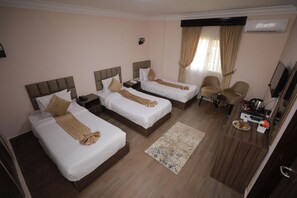 Habitación de hotel con tres camas, un escritorio con una silla, televisión y aire acondicionado.