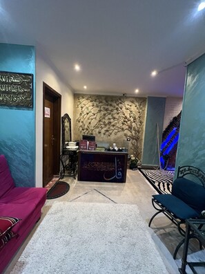 A hotel lobby with a reception desk, two chairs, a carpeted floor, and a wall with a tree mural. - Guest House Pyramids View (Giza)