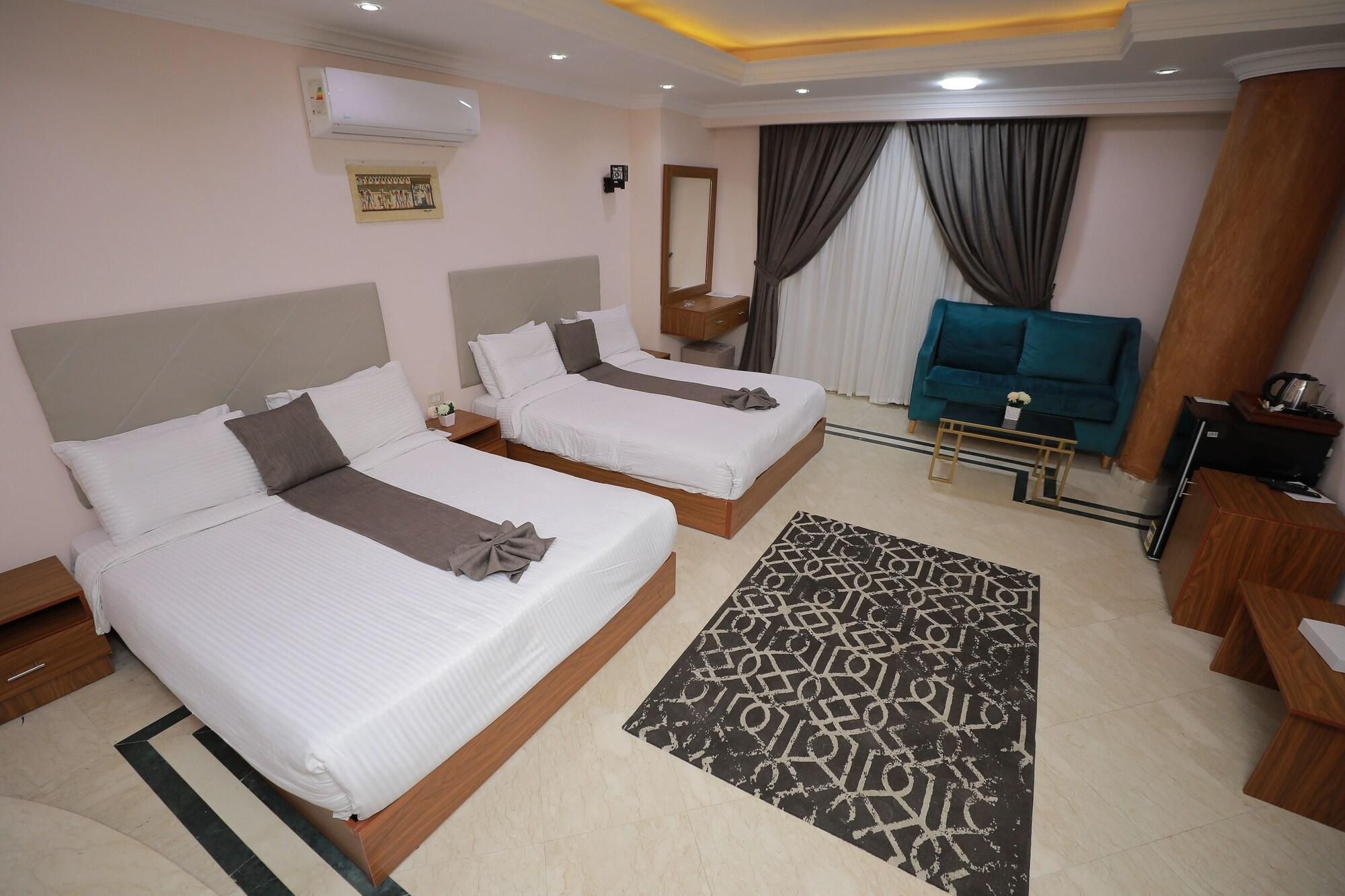 A hotel room with two beds, a TV, a sofa, a coffee table, and a patterned rug.