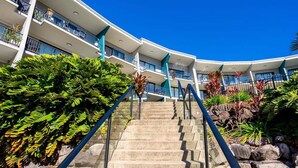 A multi-story hotel with a curved facade, outdoor stairs, and lush greenery.