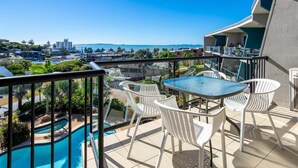 A balcony with a pool, white chairs, and a table.