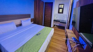 Una habitación de hotel con cama, un escritorio con televisor, un ventilador de techo y un baño pequeño.
