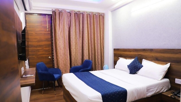 Una habitación de hotel con una cama, dos sillas, un escritorio y una cortina.