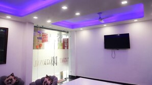 Un salón de conferencias con pared de vidrio, luces de techo, un televisor montado y un ventilador de techo.