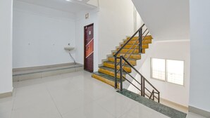 A staircase with yellow steps and black railings, a white wall with a door, and a window. - Fabhotel Ashiyana Lodge (Paud)