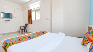 A hotel room with a bed, a TV, a chair, and a window with curtains. - Fabhotel Ashiyana Lodge (Paud)