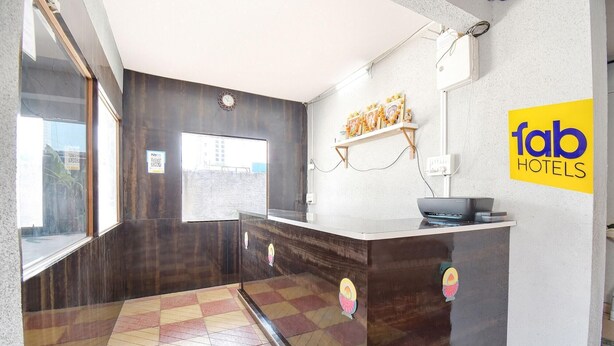 A hotel reception area with a dark wood counter, a clock, and a sign for 'fab hotels'. - Fabhotel Ashiyana Lodge (Paud)