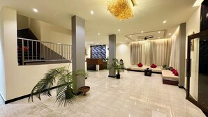 A spacious lobby with a reception desk, a staircase, a seating area with cushions, and a large chandelier. - Hotel 7 Sea S Vagator (Vagator)