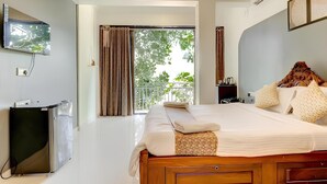 Una habitación de hotel con cama, televisión, escritorio y balcón con cortinas.