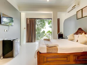 Una habitación de hotel con cama, televisión, escritorio y balcón con cortinas.