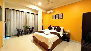 A hotel room with a large bed, a desk with a chair, a potted plant, and a sliding door leading to an outdoor area. - Hotel 7 Sea S Vagator (Vagator)