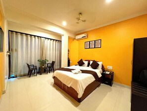 A hotel room with a large bed, a desk with a chair, a potted plant, and a sliding door leading to an outdoor area. - Hotel 7 Sea S Vagator (Vagator)